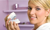a smiling blonde woman holding a fake pair of teeth